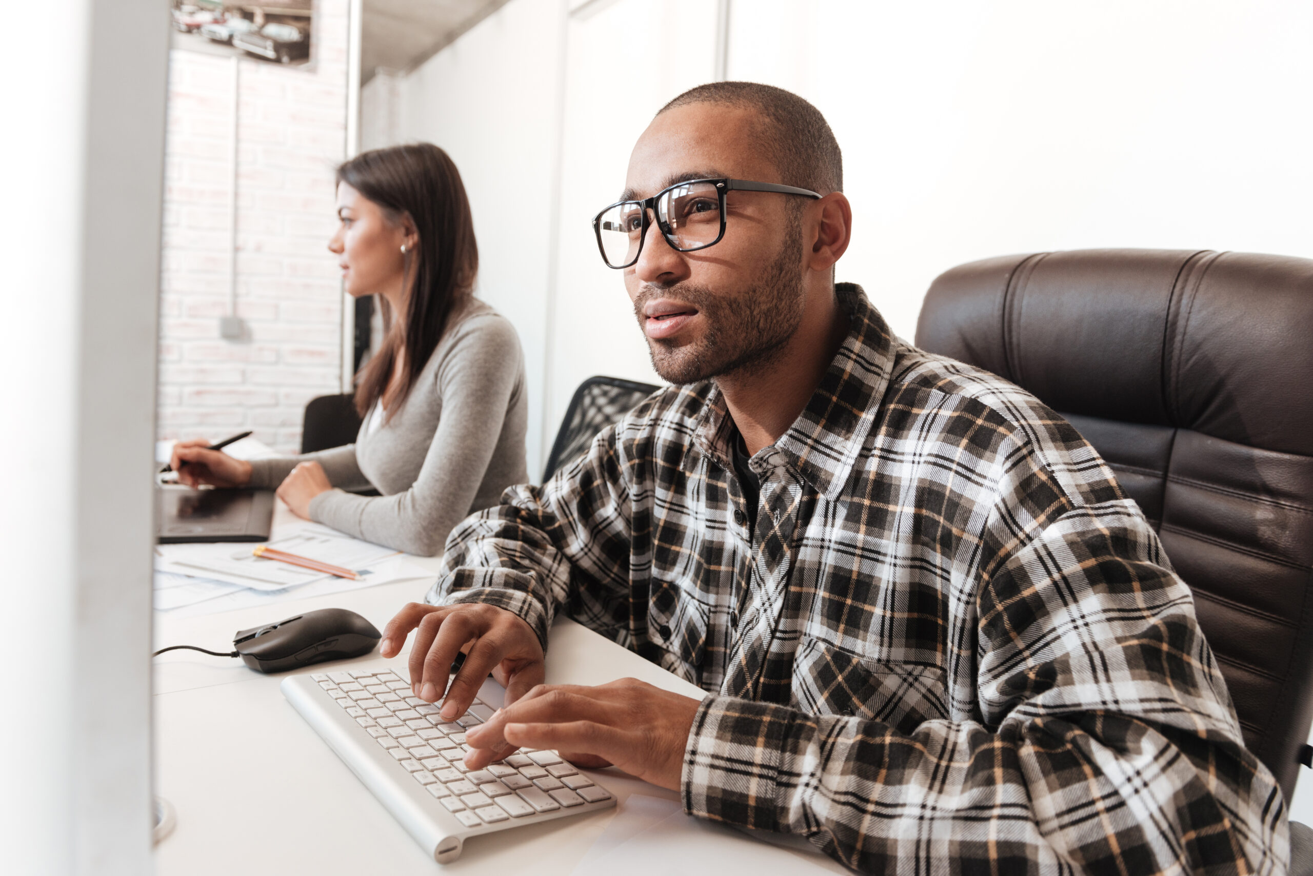 Image of young concentrated couple using computers in office. Look at computers.